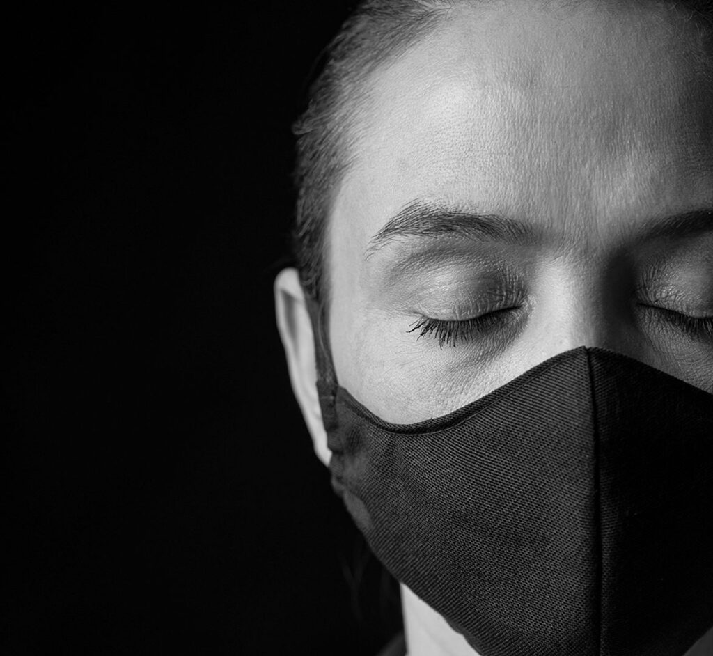 woman with a mask on and eyes closed in front of a black background