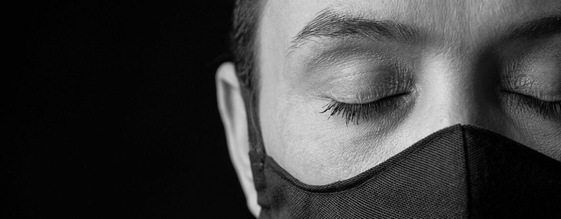 woman with a mask on and eyes closed in front of a black background