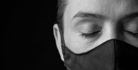 woman with a mask on and eyes closed in front of a black background