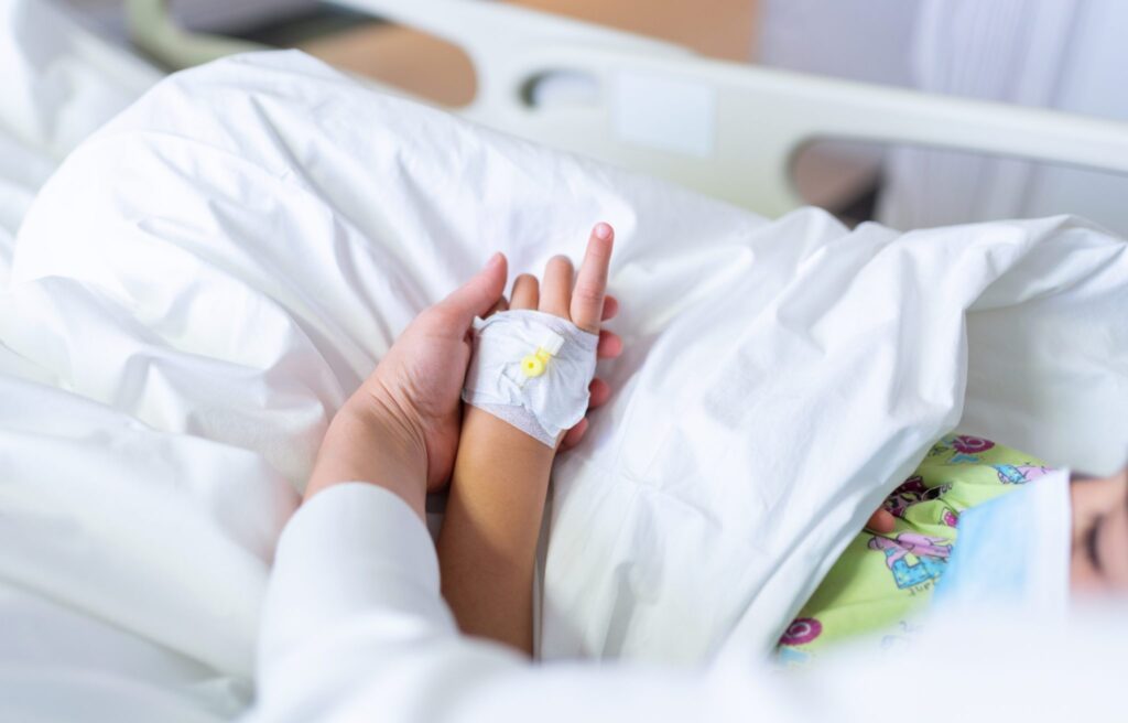 child in hospital bed with adult hand holding child's hand