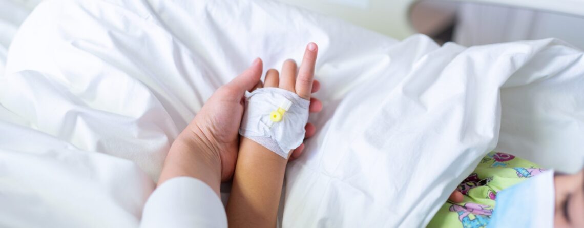 child in hospital bed with adult hand holding child's hand