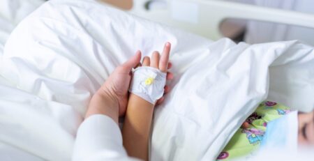 child in hospital bed with adult hand holding child's hand