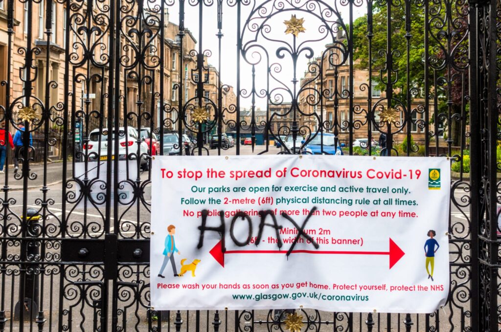 The word 'hoax' spray painted onto a banner sign communicating information about reducing the spread of covid-19 pandemic
