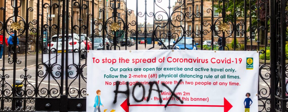 The word 'hoax' spray painted onto a banner sign communicating information about reducing the spread of covid-19 pandemic