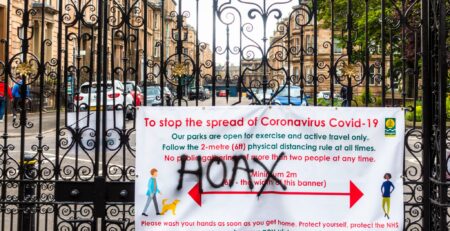 The word 'hoax' spray painted onto a banner sign communicating information about reducing the spread of covid-19 pandemic